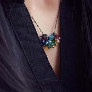 May include: A black chain necklace with a cluster of colorful glass beads. The beads are arranged in a rainbow pattern, with shades of blue, green, yellow, orange, and red.