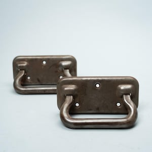 May include: Two antique-style, rectangular metal handles with a dark brown finish. Each handle has a curved, semi-circular grip and several mounting holes. The handles are likely for a cabinet or drawer.