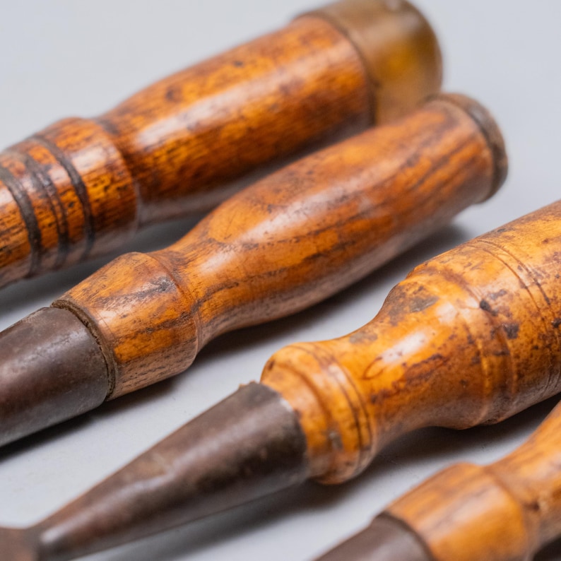 May include: Close-up of several antique wood chisels. The chisels have wooden handles with a warm, brown finish and aged metal blades. The tools are arranged at a slight angle, showcasing their craftsmanship and vintage aesthetic.