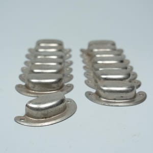 Könnte beinhalten: Eine Sammlung von elf silberfarbenen Metall-Muschelgriffen, die in zwei Reihen angeordnet sind. Jeder Griff hat ein glattes, abgerundetes, halbkreisförmiges Design mit einem flachen Befestigungsflansch auf jeder Seite und einem kleinen Loch.