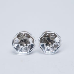 May include: Two clear, faceted glass cabinet knobs with a floral design. The knobs are round and have a silver-coloured metal base. The glass is transparent, allowing light to pass through. Suitable for furniture or cabinet upgrades.