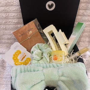 May include: A black gift box filled with beauty and self-care items. Includes a mint green headband, scrunchie, and face mask. Also features a lip balm, hair clip, and a bracelet with the words "Make a Wish".