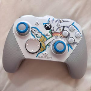 Puede incluir: Un mando Xbox Gamesir blanco y gris con un gr&aacute;fico de personaje y detalles en azul. El mando tiene joysticks y botones azules, con el logotipo de Xbox y la marca Gamesir visibles.
