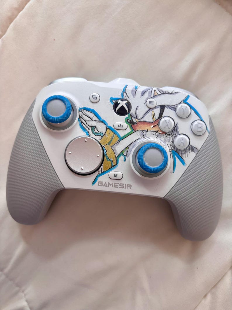 Puede incluir: Un mando Xbox Gamesir blanco y gris con un gr&aacute;fico de personaje y detalles en azul. El mando tiene joysticks y botones azules, con el logotipo de Xbox y la marca Gamesir visibles.