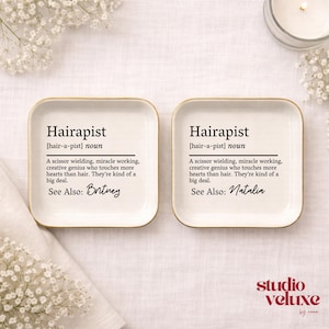 May include: Two square white ceramic trinket dishes with gold-toned rims. Each dish features black printed text defining the word Hairapist as a scissor wielding, miracle working, creative genius. One dish is personalized with Britney, the other Natalia.