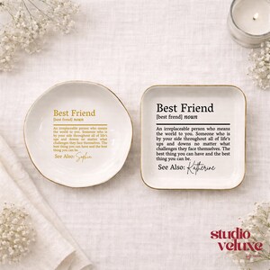 K&ouml;nnte beinhalten: Zwei wei&szlig;e Keramikschalen, eine rund und eine quadratisch, jeweils mit einer in Gold oder Schwarz gedruckten Definition eines besten Freundes. Der Text lautet: Best Friend [best frend] noun. An irreplaceable person who means the world to you.