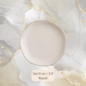 May include: A round, off-white ceramic dish with a smooth surface and a thin gold-colored rim. The dish is labeled with the text 10x10 cm / 3.9" Round, indicating its shape and dimensions of 3.9 inches in diameter for this circular object.
