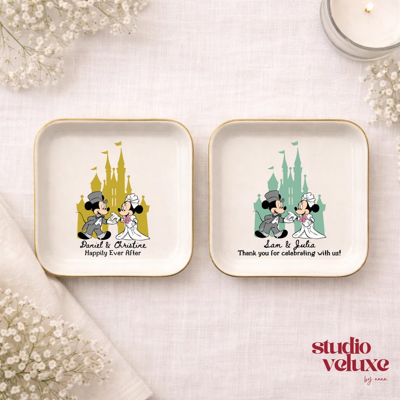 May include: Two square, white ceramic dishes with gold rims. Each features a cartoon couple in wedding attire in front of a castle. One says "Daniel & Christine Happily Ever After," the other says "Sam & Julia Thank you for celebrating with us!"