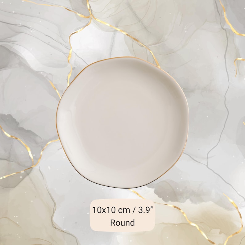 May include: A round, off-white plate with a gold rim. The plate measures 3.9 inches in diameter and has the word "Round" printed on the bottom. The plate is on a marble-like background.