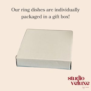 May include: A square, off-white cardboard gift box for a ring dish. The text above the box reads: Our ring dishes are individually packaged in a gift box! The text in the bottom right corner reads: studio veluxe by nana.
