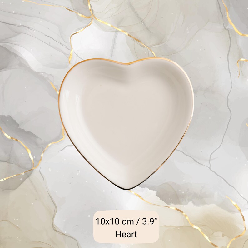 May include: A heart-shaped, off-white ceramic dish with a gold rim. The dish measures 3.9 inches in both length and width. The word "Heart" is printed below the dish.