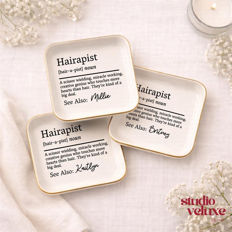 May include: Three square white ceramic trinket dishes with gold-toned rims. Each dish features black printed text defining the word Hairapist as a scissor wielding, miracle working, creative genius. Each dish includes a unique name: Millie, Britney, or Kaitlyn.
