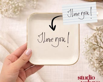 May include: A square, off-white ceramic dish with a gold rim, inscribed with "I love you" in black script. A small note with the same message is attached. The Studio Veluxe logo is visible in the bottom right corner.