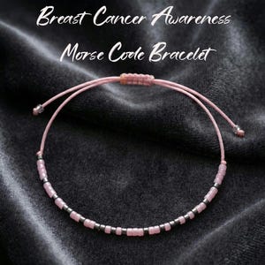 May include: Pink Morse code bracelet for Breast Cancer Awareness. The bracelet features pink beads and silver-colored spacers. The adjustable cord is pink and has silver-colored end caps. The text "Breast Cancer Awareness Morse Code Bracelet" is in the image.