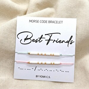 May include: Two Morse code bracelets on a white card that reads "Best Friends". The bracelets are white with gold and white beads on light green and pink string. The card also says "Morse Code Bracelet" and "BY YOMI C.S."