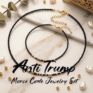 May include: A black beaded necklace and bracelet set with gold accents. The set is inscribed with the words "Anti Trump" in a cursive font, and "Morse Code Jewelry Set" in a smaller font. The jewellery is displayed on a marble surface.