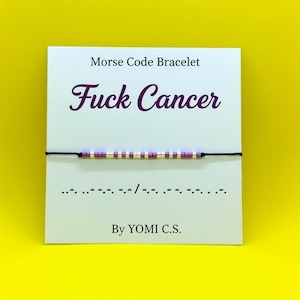 May include: A Morse code bracelet with the message "Fuck Cancer" in purple script. The bracelet features a black cord with purple and gold beads. The card also includes the Morse code translation and the name "YOMI C.S."