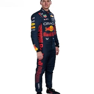 May include: A navy blue racing suit with red and yellow detailing. The suit displays sponsor logos and the Oracle logo. The Red Bull logo is visible on the chest and leg. The suit is worn with black trainers.