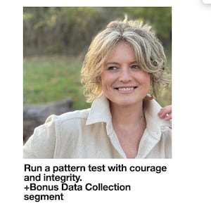 May include: A woman with blonde hair is smiling at the camera. She is wearing a light brown collared shirt. The background is blurred and appears to be a forest.