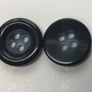 May include: Two black, round buttons with four holes each. The buttons have a glossy finish and are set against a white background. These buttons are suitable for sewing projects, clothing repair, or craft applications.