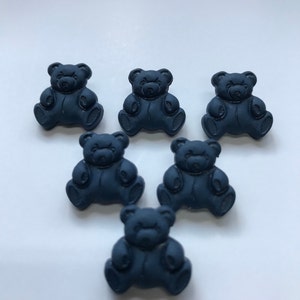 May include: Six navy blue teddy bear shaped embellishments. Each bear is sitting with its arms at its sides and has a detailed face. The bears are arranged in a semi-circle on a white surface. These are ideal for craft projects.