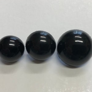 Puede incluir: Tres esferas negras brillantes de diferentes tamaños dispuestas en fila. Las esferas reflejan la luz, creando reflejos brillantes. Los diámetros son de aproximadamente 2.5, 3.8 y 5 cm.