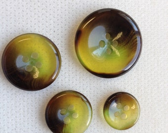 May include: Four round buttons in varying sizes, featuring a gradient of colors. The buttons transition from a dark brown outer edge to a yellow-green center. Each button has four small holes for sewing.