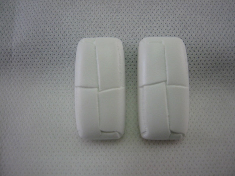 May include: Two white, rectangular objects with a textured, stitched design. The objects are positioned side-by-side against a white, dotted background. The objects have rounded edges and a segmented appearance.