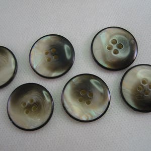 May include: Six round buttons with a pearlescent finish and four holes each. The buttons have a dark outer rim and a swirling pattern of light and dark tones, creating a subtle, elegant appearance. Ideal for sewing projects.