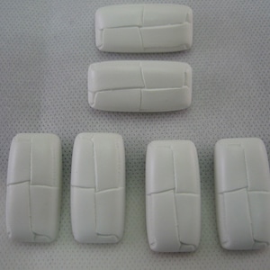 May include: A collection of six white, rectangular, ceramic tiles. Each tile has a segmented design, with lines creating a pattern across the surface. The tiles are arranged on a white, textured background.