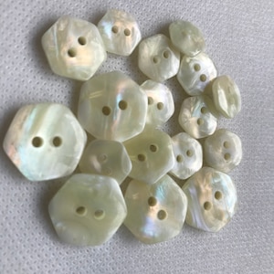 May include: A selection of iridescent, off-white buttons, hexagonal in shape. Each button features two or three holes for sewing. The buttons have a pearlescent sheen, reflecting light. Suitable for various sewing projects.