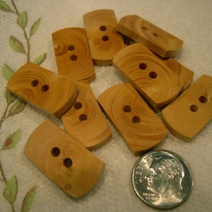 May include: A collection of light brown, rectangular wooden buttons with two holes each. The buttons have a rounded top and bottom. A US dime is included for size comparison. The buttons are likely for sewing or crafts.