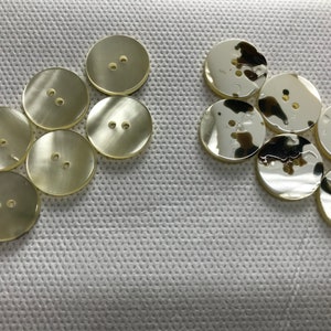 以下が含まれることがあります： 丸く明るい色のボタンのコレクションで、それぞれに2つの穴があります。滑らかで反射する表面を持つボタンもあれば、テクスチャ加工されたまだら模様のボタンもあります。ボタンは白いテクスチャ加工された生地の上に配置されています。