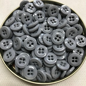 Peut inclure: Un ensemble de boutons gris à quatre trous dans un récipient en métal. Les boutons ronds ont une finition brillante. Les boutons sont d'une couleur neutre unie, adaptés à divers projets de couture. Les boutons sont dispersés dans le récipient.