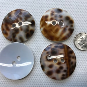 May include: Four large buttons with two holes each. Two buttons have a brown and cream tortoiseshell pattern, one is solid light gray, and the last has a brown and cream pattern. A US dime is included for size comparison.