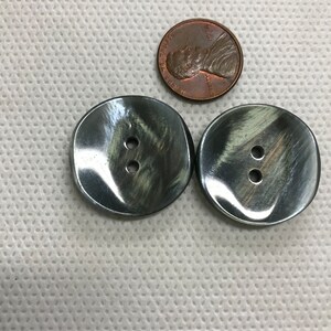 K&ouml;nnte beinhalten: Zwei gro&szlig;e, dunkelgraue Kn&ouml;pfe mit je zwei L&ouml;chern, neben einem Kupferpfennig. Die Kn&ouml;pfe haben einen leicht irisierenden Glanz. Die Kn&ouml;pfe sind rund mit einer leicht unregelm&auml;&szlig;igen Form. Die M&uuml;nze ist eine M&uuml;nze.
