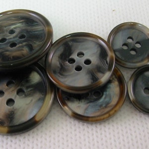 May include: A selection of six round buttons in different sizes. The buttons have a marbled effect with shades of brown, black, and cream. Each button has four holes for sewing. Suitable for clothing and craft projects.