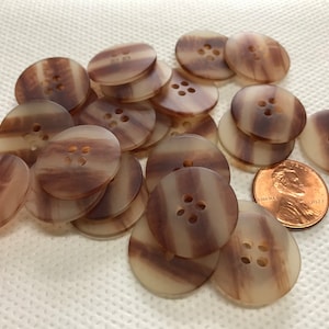 May include: A collection of round, brown and cream-colored buttons with four holes each. The buttons have a striped pattern and are scattered on a white surface. A penny is included for size reference.