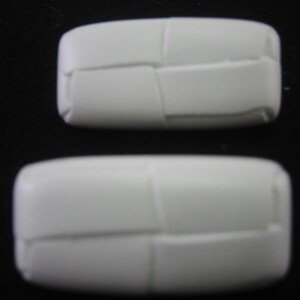 May include: Two white, rectangular objects with a woven texture are displayed against a black background. The objects are rounded at the edges and appear to be made of a solid material. The larger object is positioned below the smaller one.