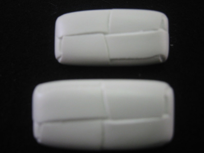May include: Two white, rectangular objects with a woven texture are displayed against a black background. The objects are rounded at the edges and appear to be made of a solid material. The larger object is positioned below the smaller one.