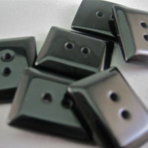 May include: A collection of glossy, dark gray rectangular buttons. Each button has two small holes for sewing. The buttons have a slightly rounded shape and a smooth, reflective surface, suggesting a formal or classic style.