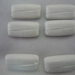May include: Six white, rectangular ceramic tiles with a textured, segmented design. The tiles are arranged in two rows, with three tiles in the top row and three in the bottom row. The tiles are on a white surface.