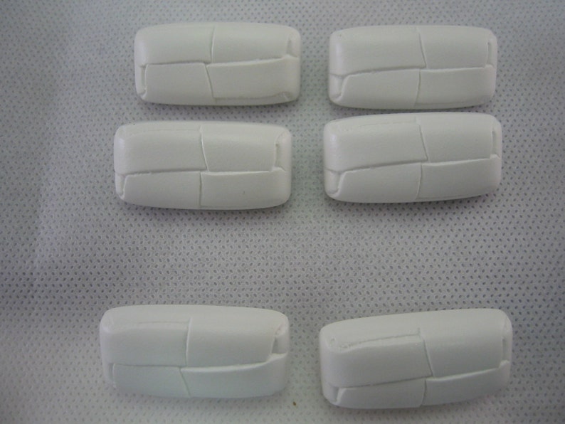 May include: Six white, rectangular ceramic tiles with a textured, segmented design. The tiles are arranged in two rows, with three tiles in the top row and three in the bottom row. The tiles are on a white surface.