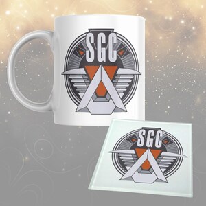 May include: White ceramic mug and glass coaster set. The design features the letters "SGC" in a bold font, with a geometric design in grey, orange, and white. The mug has a curved handle. The coaster is square.