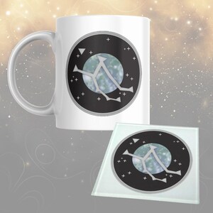 May include: A white ceramic mug and a glass coaster with a celestial design. The design features a black circle with a light blue planet-like sphere, white star-like shapes, and a white geometric figure. The mug has a curved handle.
