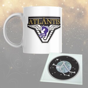 May include: White ceramic mug featuring the word "ATLANTIS" in gold, a purple horse graphic, and a glass coaster with a celestial design. The mug has a large handle.