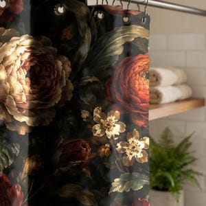 May include: A shower curtain featuring a dark, moody floral pattern with large, layered cream and deep red roses, smaller white blossoms, and dark green foliage. The curtain is suspended from a metal rod by circular metal grommets.