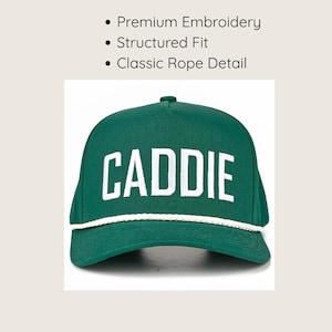 May include: A forest green baseball cap featuring the word CADDIE embroidered in white capital letters across the front. The cap has a structured fit and a white braided rope detail running horizontally across the base of the crown.
