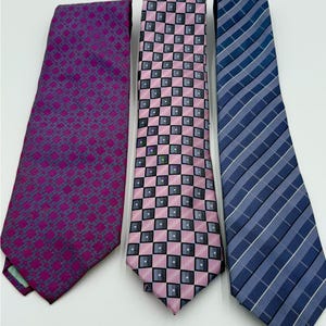 May include: Three neckties with different patterns. The first tie is a deep purple with a repeating geometric design. The second tie is pink with a checkered pattern of black and gray squares. The third tie is blue with white stripes.