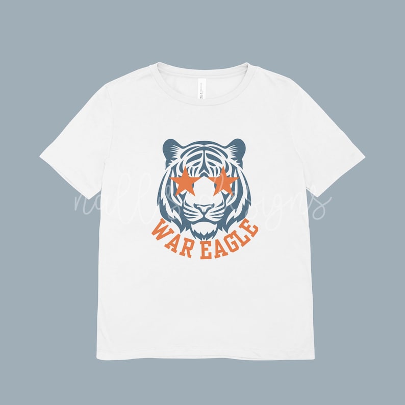 May include: White t-shirt featuring a tiger graphic with orange star-shaped sunglasses and the text "WAR EAGLE" in orange. The tiger is blue and white. The shirt is a classic crew neck.